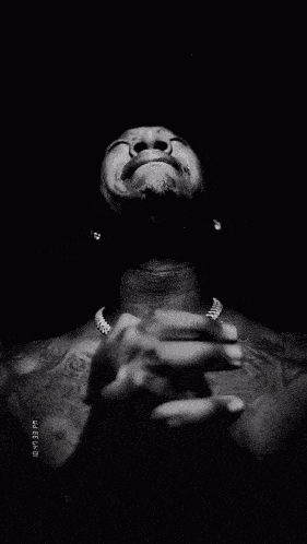 a black and white photo of a shirtless man with his hands folded in front of his face